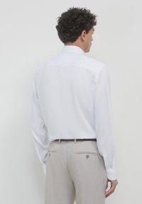 Chemise blanche à manches longues avec un col classique, texture lisse et poignets boutonnés, associée à un pantalon beige clair sur mesure avec poches.