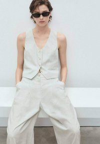 To-delt outfit bestående af en lys grå, ribbet vest med knapper og matchende vide bukser med lommer, struktureret stof.