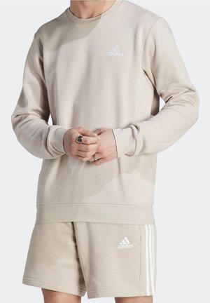 Beige bomulds-sweatshirt med rund hals, lange ærmer og ribbede manchetter. Har et lille hvidt Adidas-logo på brystet.
