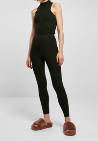 Svart ribbad tajt linne och matchande högmidjade leggings, i kombination med bruna lurviga tofflor. Slät textur överallt.