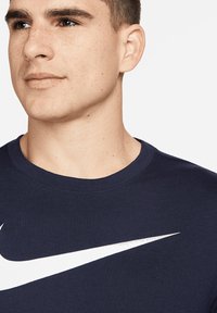 Navyblaues T-Shirt mit kurzen Ärmeln aus Baumwolle und geripptem Rundhalsausschnitt. Mit einem großen weißen Nike-Swoosh-Logo über der Brust.