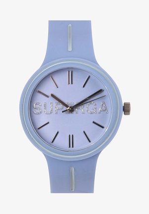 Reloj de silicona azul con esfera redonda, marcadores de hora plateados y un logo "SUPERGA" en detalle brillante sobre un fondo mate lavanda.