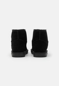 Zwarte suede enkelboots met een gestructureerde afwerking, afgeronde achterkant en platte rubberen zolen. Naaddetails dragen bij aan het ontwerp.