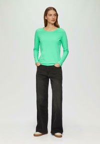 Minta zelena majica s dugim rukavima i okruglim izrezom, uparena s crnim hlačama širokih nogavica i kremastimtenisicama s smešnim đonom.