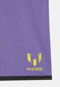 Lilla treningsskjorte med en gul logo og teksten "MESSi" nederst. Svart kant langs nederkanten gir kontrast. Glatt tekstur.