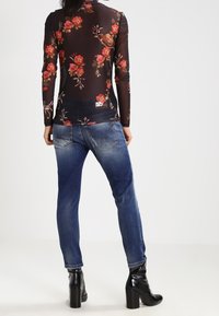 Top nero trasparente a maniche lunghe con motivo floreale, abbinato a jeans blu e stivali neri lucidi alla caviglia. L'outfit presenta silhouette aderenti.