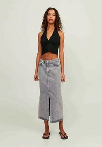 Black halter crop top paired with a high-waisted, knee-length denim skirt featuring a front slit. Model wears black flip-flops.