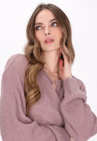 Cárdigan de punto en color rosa claro con una textura suave, que presenta un escote en V y mangas sueltas y oversize, usado de forma casual.