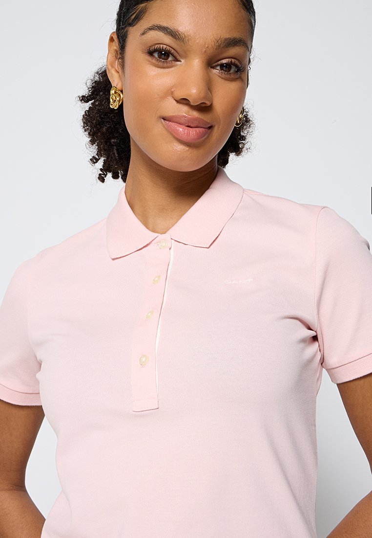 Polo shirt rose clair en tissu texturé, fermeture à trois boutons et logo subtilement brodé sur la poitrine. Manches courtes.