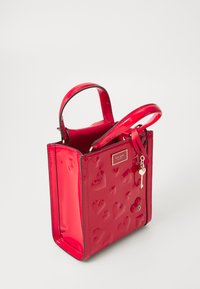 Rode patenten leren tote bag met verhoogd hartpatroon, bovenhandvaten en een sleutelhangertje als accent. Vierkante vorm met een gladde textuur en metalen logo.