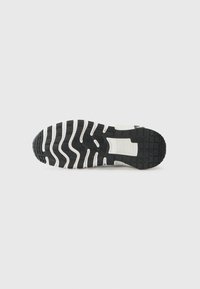 Sneakersål i sort og hvid med et struktureret gummimønster, der har riller og forhøjninger for godt greb; overvejende sort med hvide accenter.