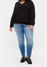 Blouse noire à manches longues et col en V, associée à un jean skinny en denim bleu. La blouse présente une coupe décontractée ; le jean a une finition délavée. Mocassins à plateforme noirs.