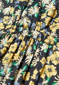 Mustaa kangasta, jossa on kukkakuosi, joka sisältää keltaisia ja harmaita kukkia, vihreit�ä lehtiä ja rypytystä vyötäröalueella.