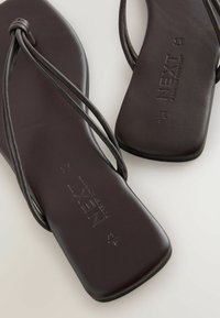 Sandali piatti marroni con cinturini sottili, texture liscia e logo in rilievo sulla soletta. Presentano una soletta sagomata per il comfort.