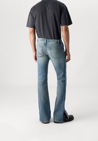 Jeans ajustados de color azul claro con un desvanecimiento sutil, cinco bolsillos y cremallera. Combinados con una camiseta de manga corta gris oscuro y calzado negro.