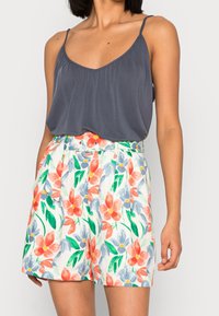 Grå ärmlös topp med V-ringning, kombinerad med blommönstrade shorts som har rosa, blått och grönt på en ljus bakgrund.