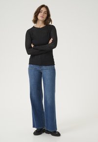 Haut noir à manches longues avec un motif texturé, associé à un jean bleu à jambes larges. L'ensemble comprend des chaussures noires et présente un col rond.