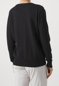 Svart stickad tröja med ribbad krage och muddar. Mjuk textur, avslappnad passform och rak nederkant som visar en enkel, ren design.