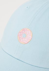Casquette bleue en coton avec un design structuré présentant un donut rose brodé à l'avant. Le matériau a une finition texturée.