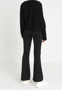 Maglione nero con texture, a vestibilità ampia e maniche lunghe, abbinato a pantaloni neri svasati e sneakers bianche, visto da dietro.