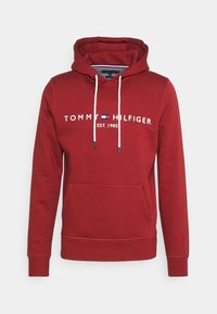 Sudadera roja de Tommy Hilfiger con cordones blancos, bolsillo frontal y texto del logo "TOMMY HILFIGER EST. 1985" en el pecho.