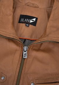 Braune Lederjacke mit silbernem Reißverschluss, ausgestattet mit einem Etikett "JILANI COLLECTION" und zwei Fronttaschen mit Druckknopfverschluss.