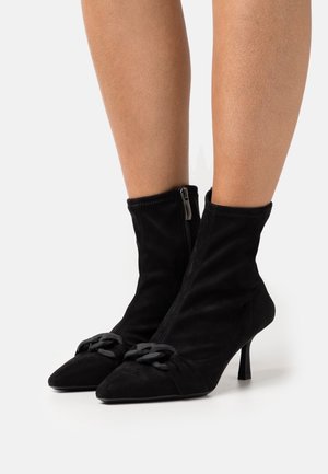 Svarta ankelboots i mocka med spetsig tå, medelhög klack och dekorativ kedjedetalj framtill. Har en sidoförslutning med dragkedja.