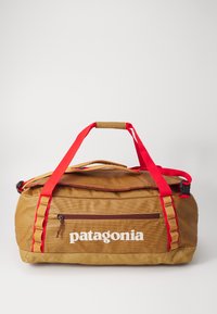 Brown Patagonia duffel bag with red straps, front zipper pocket, and padded handle on a plain white background.