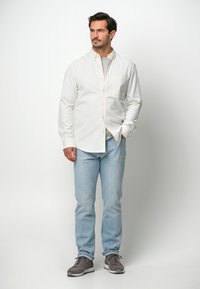 Witte button-up overhemd met lange mouwen, lichtblauwe spijkerbroek en grijze sneakers. Het overhemd heeft een borstzak en een klassieke kraag.
