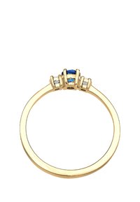 Anillo de oro con una gema azul central flanqueada por dos piedras transparentes, con una banda lisa y engastes de garra detallados.