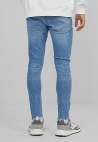 Jeans skinny azul claro con dobladillo desgastado, que presentan un ajuste clásico y cinco bolsillos, combinados con zapatillas grises y blancas.