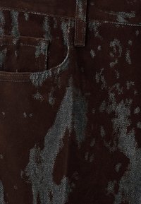 Țesătură de denim maro cu un model subtil, texturat și accente gri mai deschise; include un buzunar cusut și un talie.