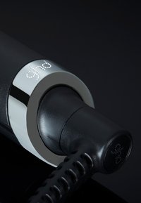 Zwart haarstylingshulpmiddel met digitale "ghd" weergave op zilveren ring en gestructureerde zwarte kabel uiteinde op donkere achtergrond.