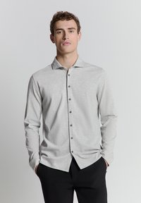 Lichtgrijze langdrieke button-up shirt met een zachte textuur, een klassieke kraag en donkere knopen aan de voorkant, gecombineerd met zwarte broeken.