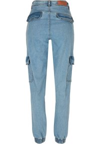 Pantalon cargo en denim bleu clair avec poignets élastiques, poches à rabat à l'arrière et sur les côtés, et un patch en cuir marron sur la ceinture.