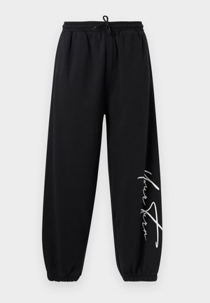 Zwarte sweatpants met elastische tailleband, enkellinten en witte cursieve tekst op het rechterbeen.