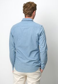  Lichtblauw, lang mouw, knoopsluiting overhemd met een zachte textuur. Afgeronde zoom en manchetten met één knoop. G gedragen met crèmekleurige broek.