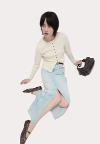 Cardigan a coste crema con bottoni, gonna di denim azzurro chiaro con uno spacco laterale e ballerine nere con stampa leopardata. Borsa marrone con tracolla.