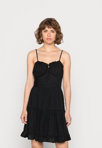 Vestido preto com corpete ajustado com detalhes franzidos, alças ajustáveis, uma abertura em forma de olho de fechadura e uma saia em camadas e larga.