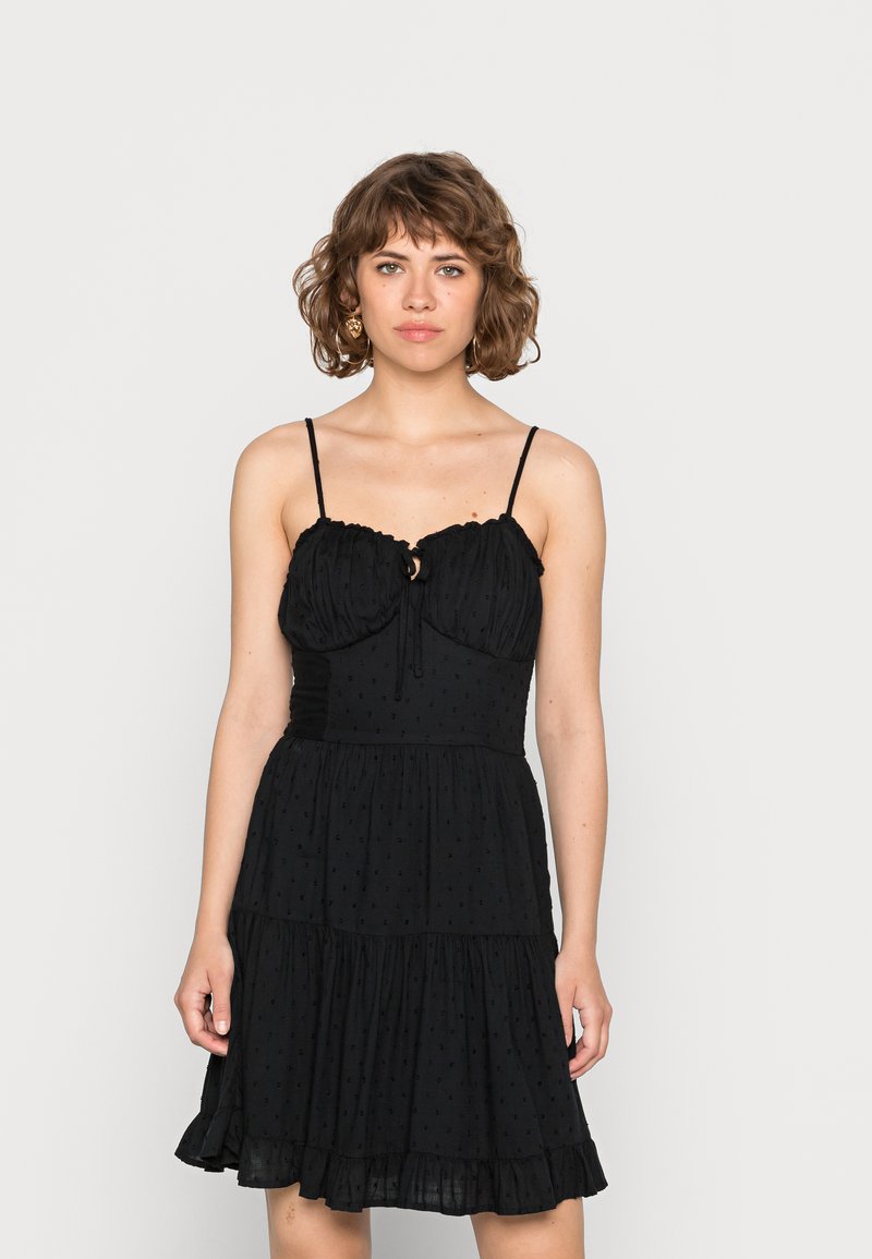 Vestido preto com corpete ajustado com detalhes franzidos, alças ajustáveis, uma abertura em forma de olho de fechadura e uma saia em camadas e larga.