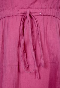 Fuchsiová látka s texturovaným povrchem, s elastickým pasem a dvěma dlouhými šňůrkami, čímž vytváří nařasený design.
