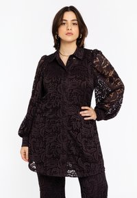 Zwarte kanten blouse met lange pofmouwen, knoopsluiting aan de voorkant, bloemenpatroon en licht uitlopende zoom. Geaccentueerd met een doorzichtige textuur.