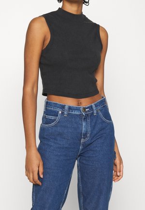Crop top sans manches noir à côtes avec un col haut, associé à un jean en denim bleu taille haute avec poches avant et accents en métal.