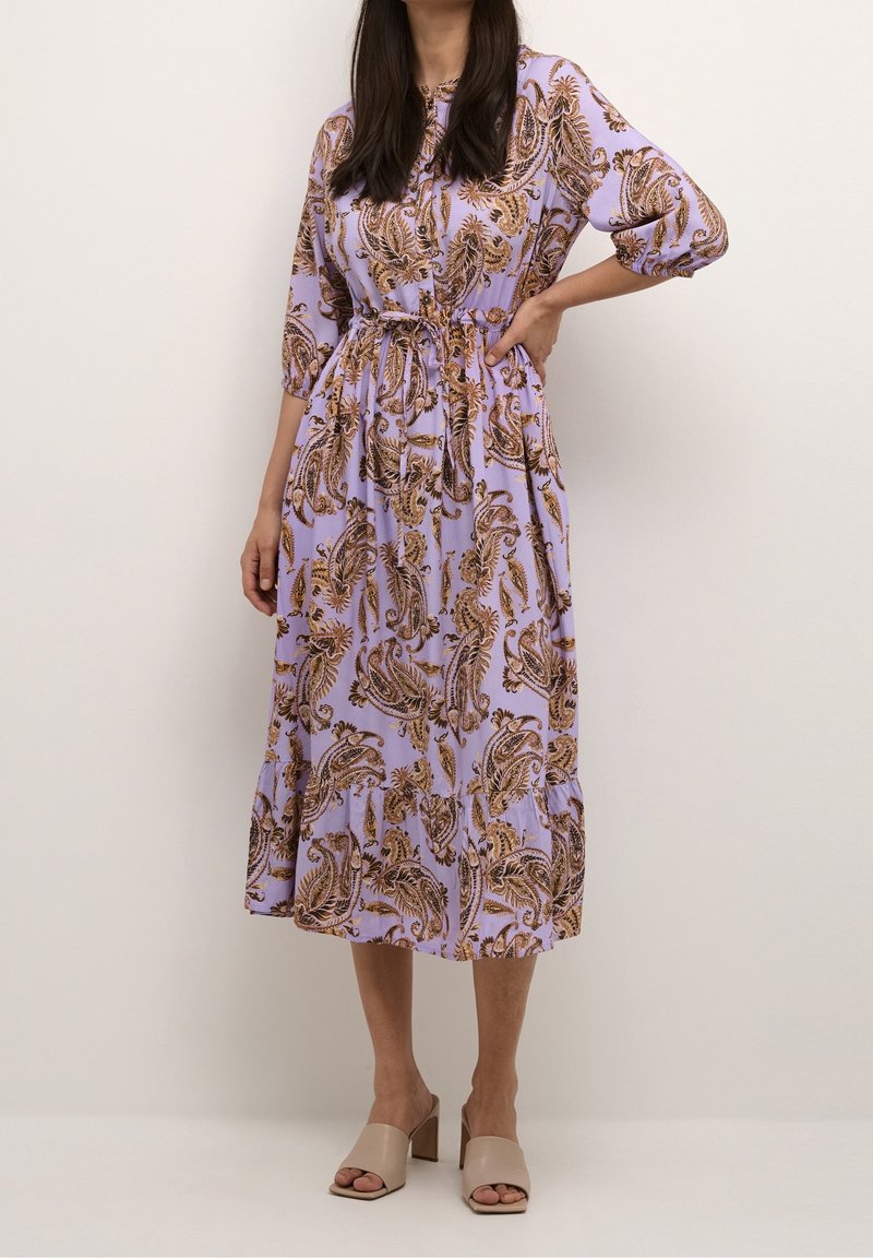 Fialové maxi šaty s paisley vzorem v hnědé a zlaté barvě. Mají tříčtvrteční rukávy, zúžený pas a stufenovaný lem.