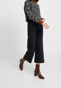 Maglione leopardato con colletto a coste marrone, abbinato a pantaloni neri a gamba larga e stivaletti alla caviglia marroni in texture con tacco a blocco.
