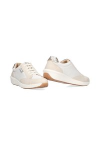 Zapatillas beige y blancas con un acento metálico en el talón, fabricadas con tejido texturizado y suela de goma. Cuentan con cordones y cuellos acolchados.