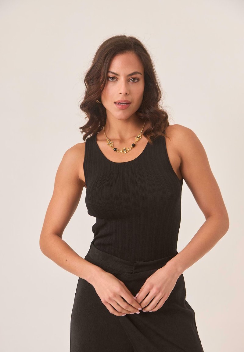 Top de tirantes negro con escote redondeado. Combinado con pantalones de talle alto negros con textura y collar llamativo dorado.