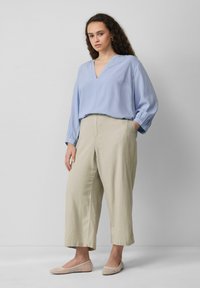 Lichtblauwe blouse met lange mouwen en een V-hals, gecombineerd met beige palazzo-pantalons en lichte mesh flats. Eenvoudig ontwerp, zachte stof en neutrale kleuren.