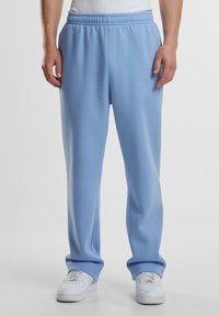 Lyseblå sweatpants lavet af blødt stof, med elastisk talje, lige ben og en afslappet pasform. Parret med hvide sneakers.