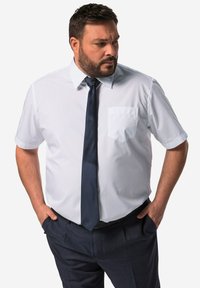 Camicetta bianca a maniche corte con taschino sul petto, abbinata a una cravatta blu scuro e pantaloni. Tessuto morbido, vestibilità su misura e elementi di design semplici.
